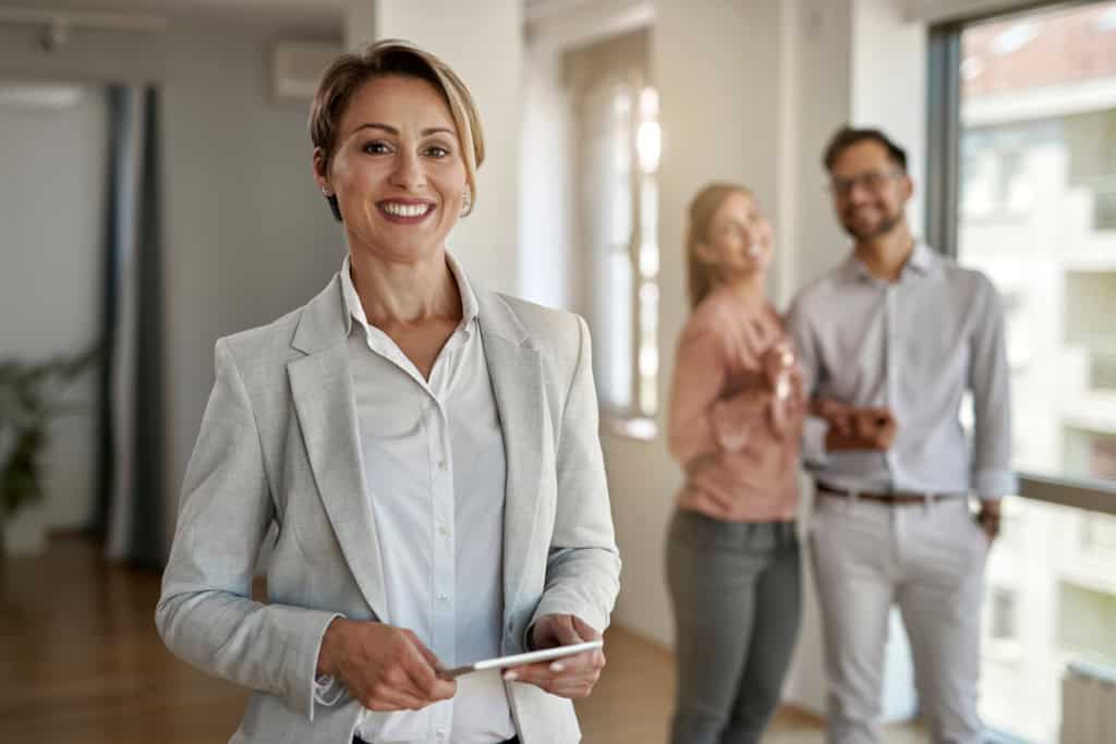 An agent smiling while buyers tour a home, on the number one trait to look for in a real estate broker