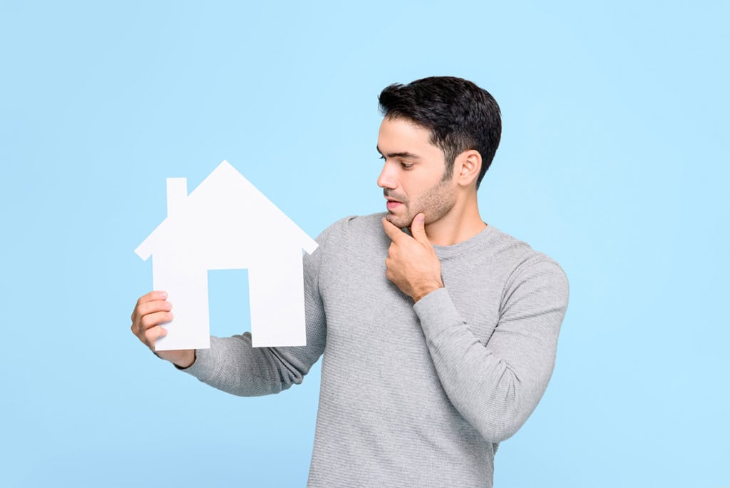 A man holding a paper house in thought, on not underestimating the cost of ownership