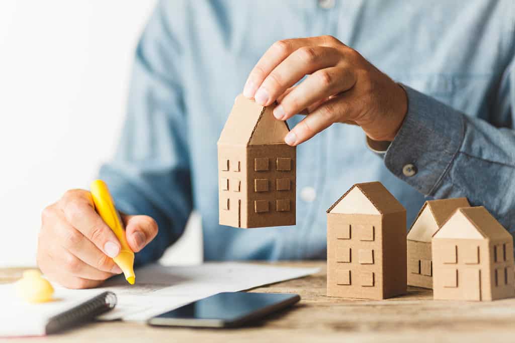 An investor arranging model houses while taking notes, on buying a rental property sight unseen